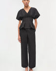 Woman wearing a black peplum top and wide-leg pants on a white background