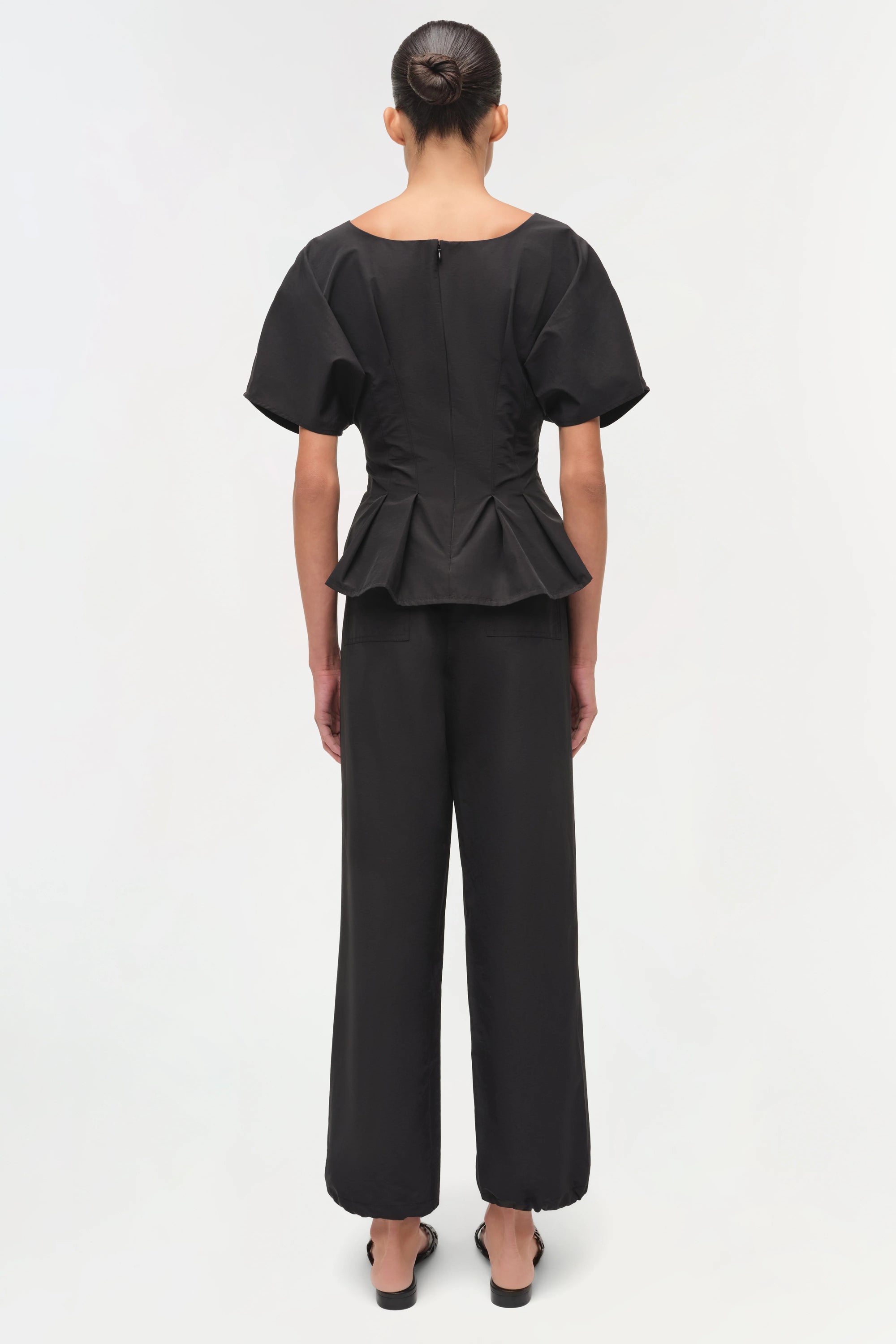 Person wearing a black peplum top and wide-leg pants on a white background