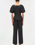Person wearing a black peplum top and wide-leg pants on a white background