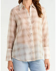 A woman wearing a long-sleeve button-up shirt with a soft beige and light brown plaid pattern, paired with light blue jeans, against a plain white background.