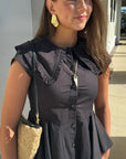 Woman wearing a black peplum top with lace details, holding a beige handbag.