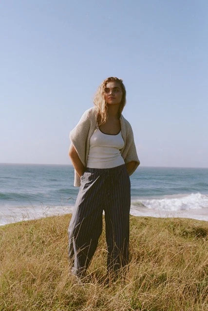 Woman standing on a grassy hill by the ocean with a clear sky.