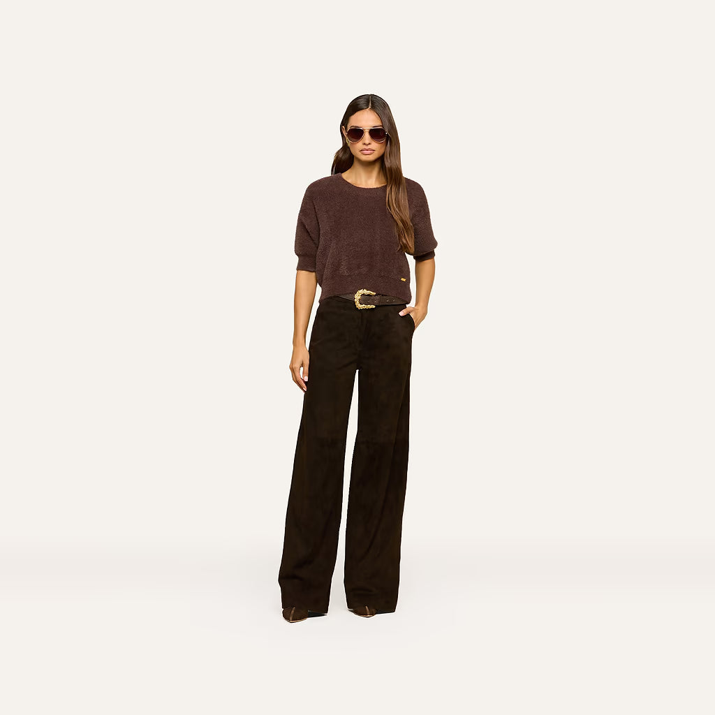 A woman modeling a dark brown short-sleeve knit top and dark brown wide-leg pants with a gold-tone belt, standing against a solid off-white background.