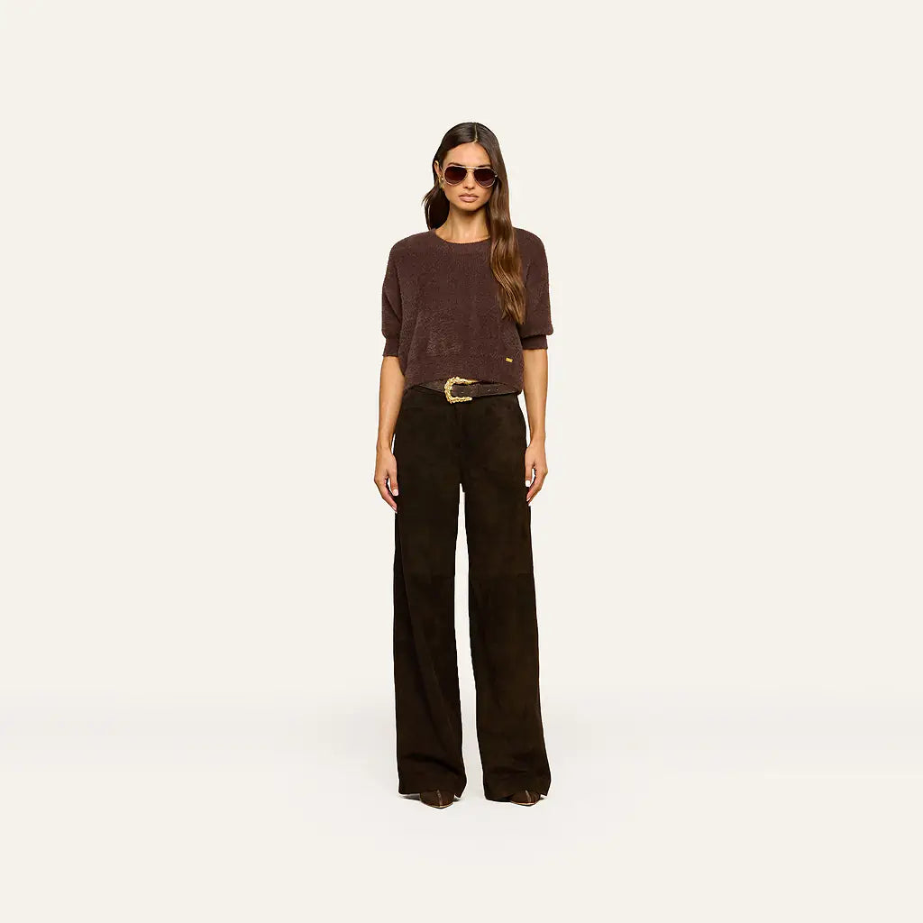 A woman wearing a brown fuzzy cropped sweater and dark brown wide-leg pants, set against a plain off-white background.