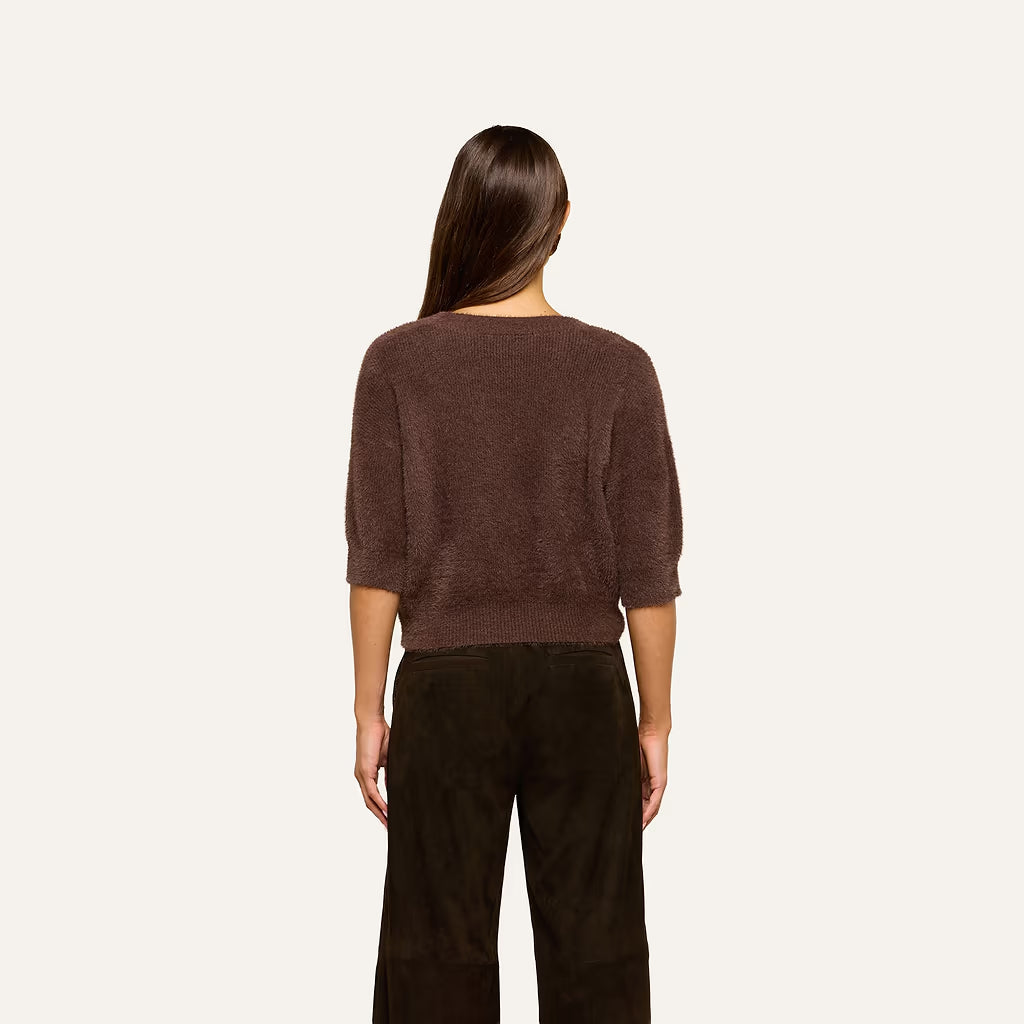 A woman viewed from the back wearing a brown fuzzy cropped sweater and dark brown wide-leg pants, set against a plain off-white background.