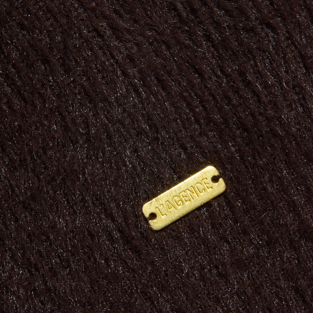 A close-up of dark brown textured fabric with a small rectangular gold-tone metal tag engraved 