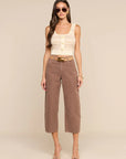 A woman modeling a cream ribbed knit cropped tank top with gold buttons and brown wide-leg cropped pants with a tan belt, set against a solid beige studio background.