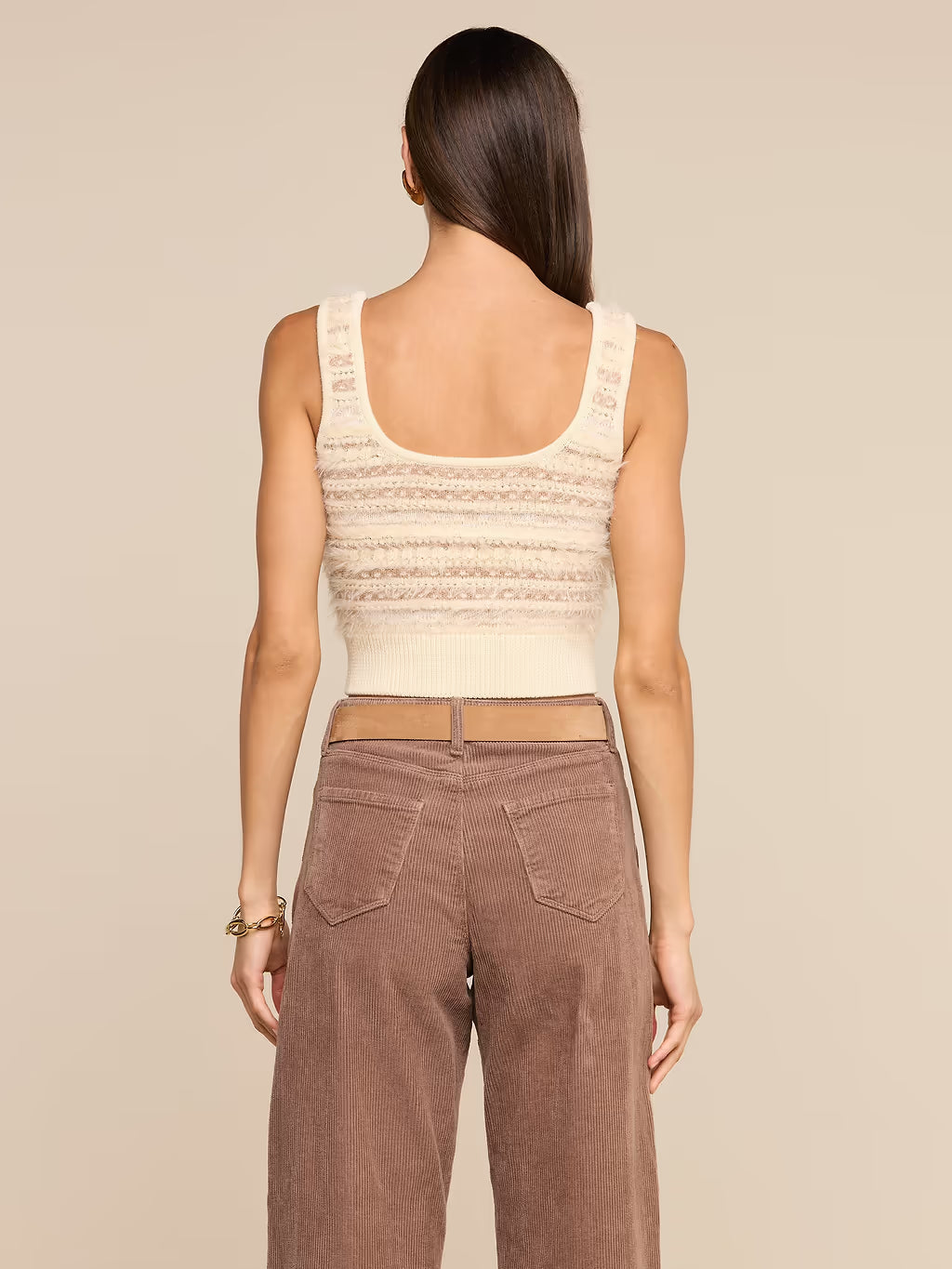 A woman shown from the back wearing a cream knit cropped tank top and brown wide-leg pants, against a solid beige studio background.