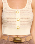 A close-up of a person wearing a cream-colored textured knit crop top with three gold buttons, paired with a tan belt and brown corduroy pants.