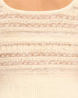 Close-up of a cream-colored knit sweater with textured horizontal stripes and a ribbed crew neck.