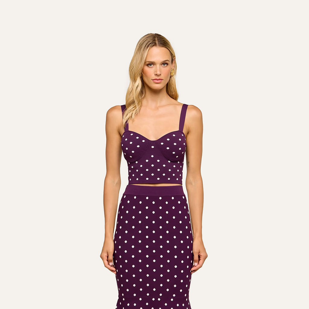 A blonde model wearing a matching two-piece knit set consisting of a purple crop top and skirt with a white polka dot pattern, set against a solid off-white background.