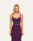 A blonde model wearing a matching two-piece knit set consisting of a purple crop top and skirt with a white polka dot pattern, set against a solid off-white background.