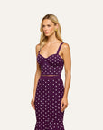 A woman modeling a two-piece sleeveless dress set in deep purple with a white polka dot pattern, featuring a structured sweetheart bustier top and a matching high-waisted skirt, set against a solid off-white background.