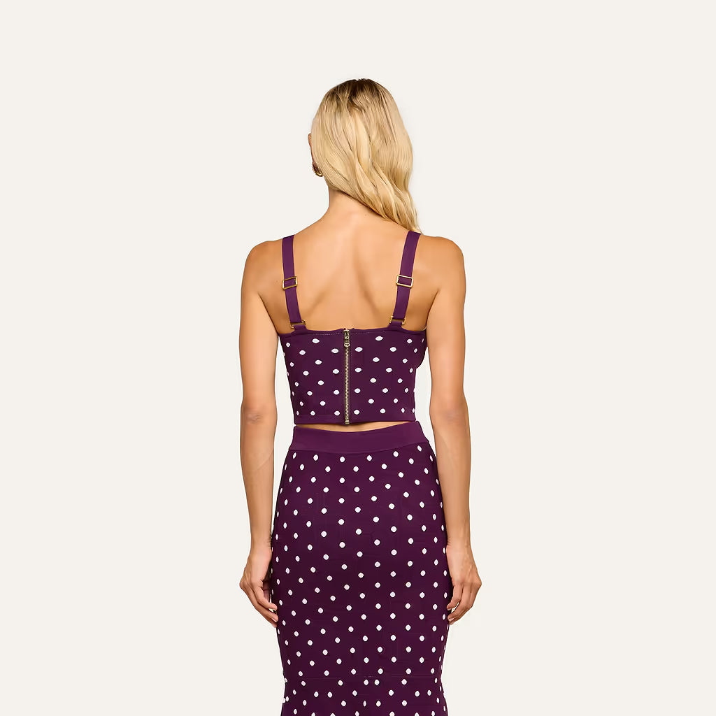 A woman viewed from the back wearing a purple and white polka dot two-piece set consisting of a crop top with shoulder straps and a matching high-waisted pencil skirt, against a solid off-white background.