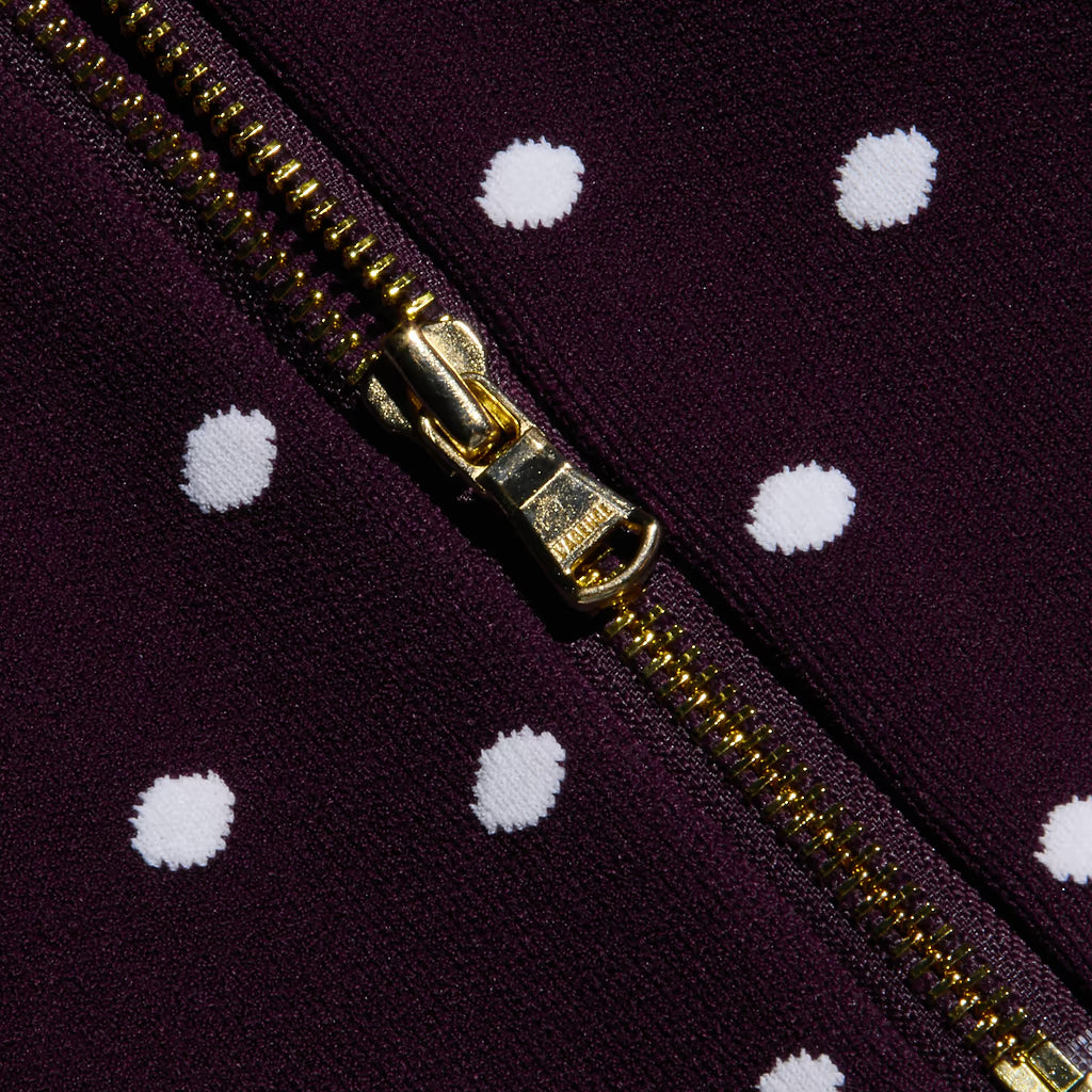 Close-up of a gold zipper on a dark purple fabric with white polka dots.