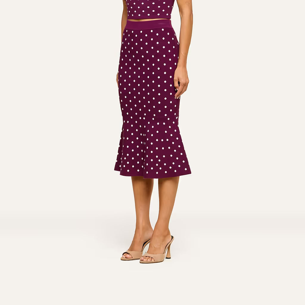 A model wearing a dark purple midi skirt with white polka dots and beige heeled sandals, shown from the waist down against a light off-white background.
