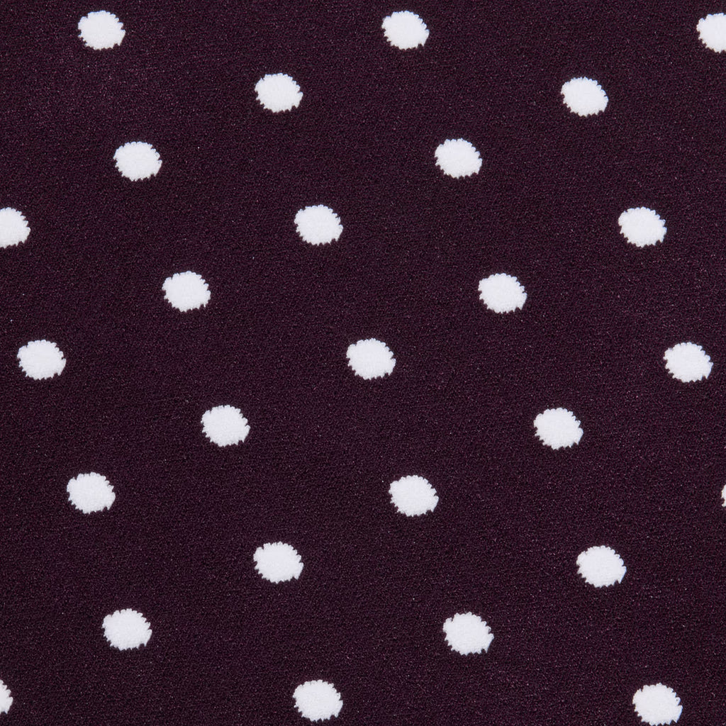A close-up of a dark plum purple textured fabric with a repeating pattern of white polka dots.