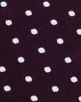 A close-up of a dark plum purple textured fabric with a repeating pattern of white polka dots.
