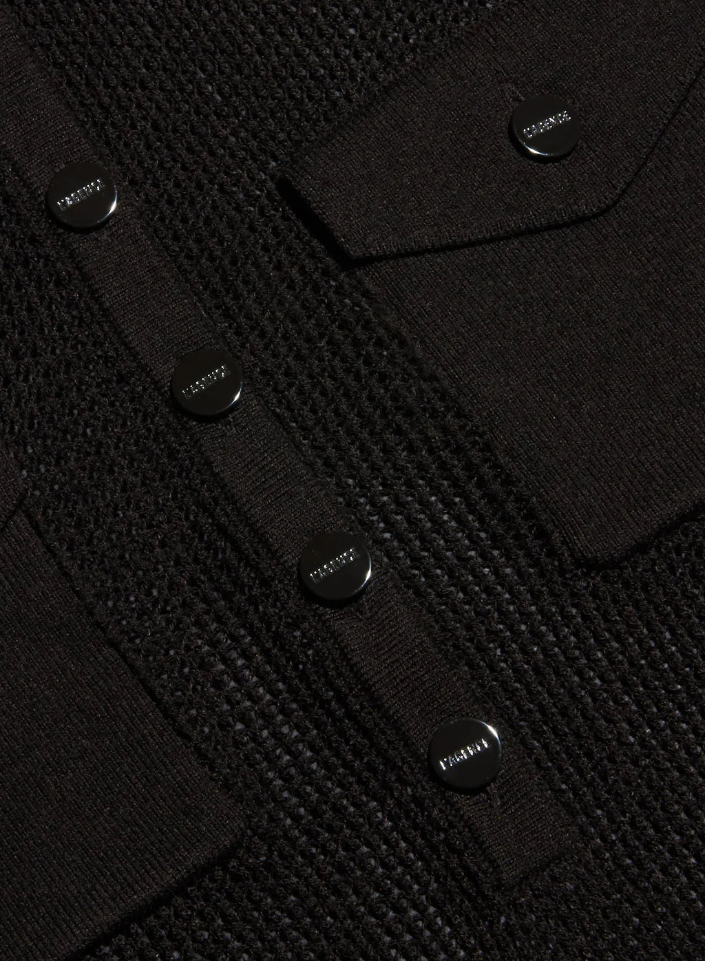 Close-up of a black textured knit cardigan featuring a buttoned chest pocket and matching buttoned flap pockets, with the brand name 'LAGENCE visible on the buttons.