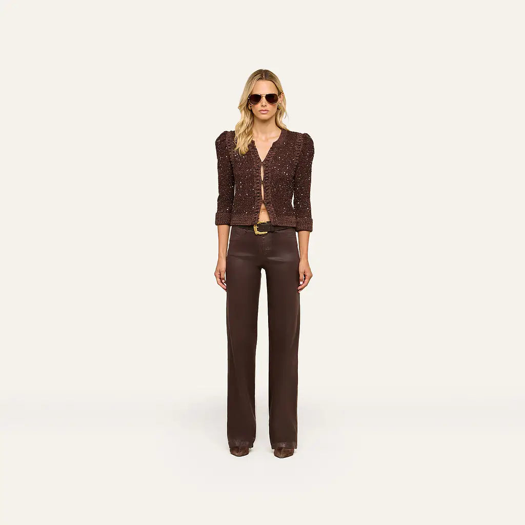 A model stands against a plain off-white studio background wearing a dark brown textured three-quarter sleeve jacket with puffed shoulders and matching dark brown wide-leg trousers.