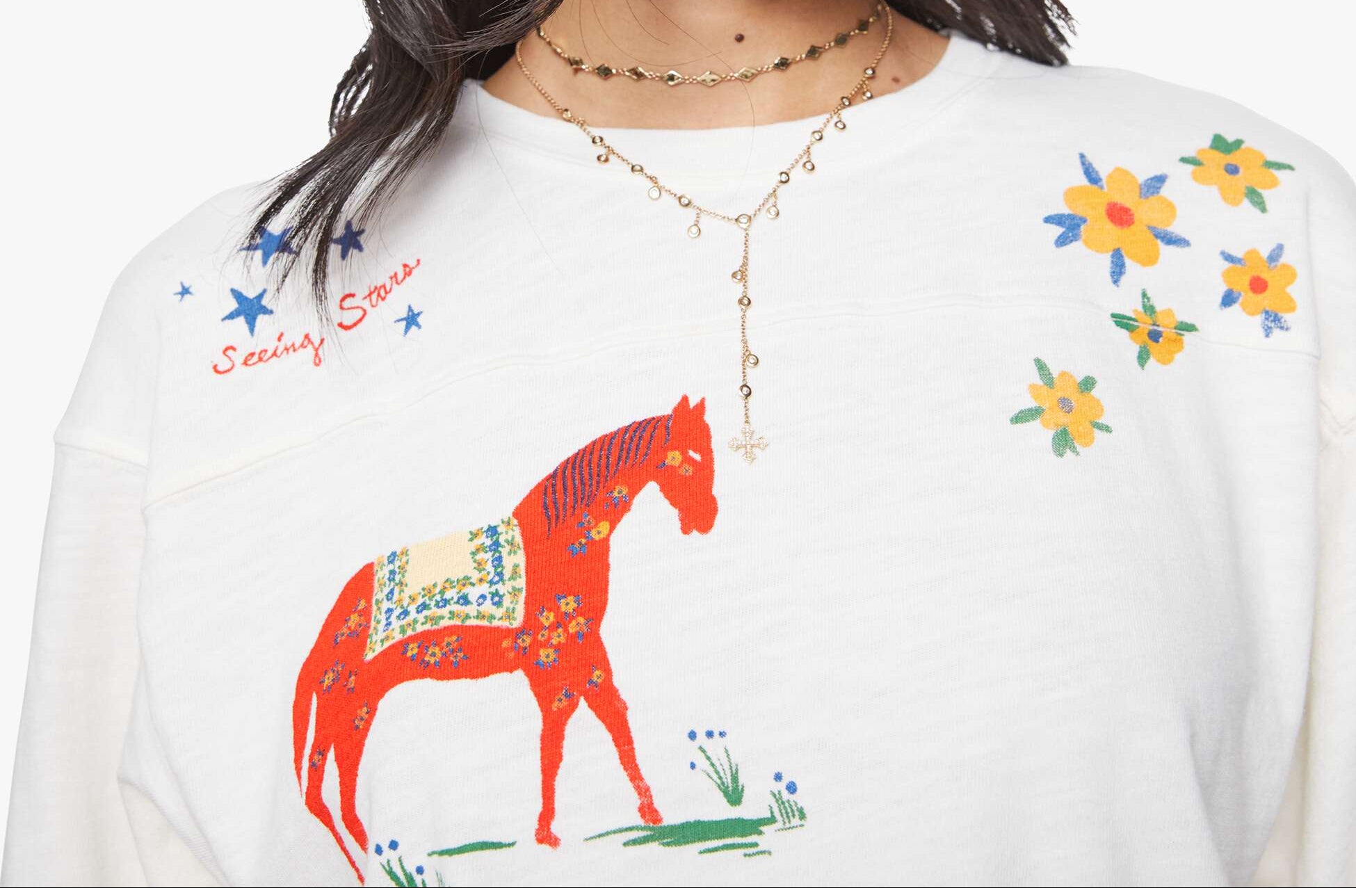 Woman wearing sunglasses and a white shirt with a colorful horse design on a plain background
