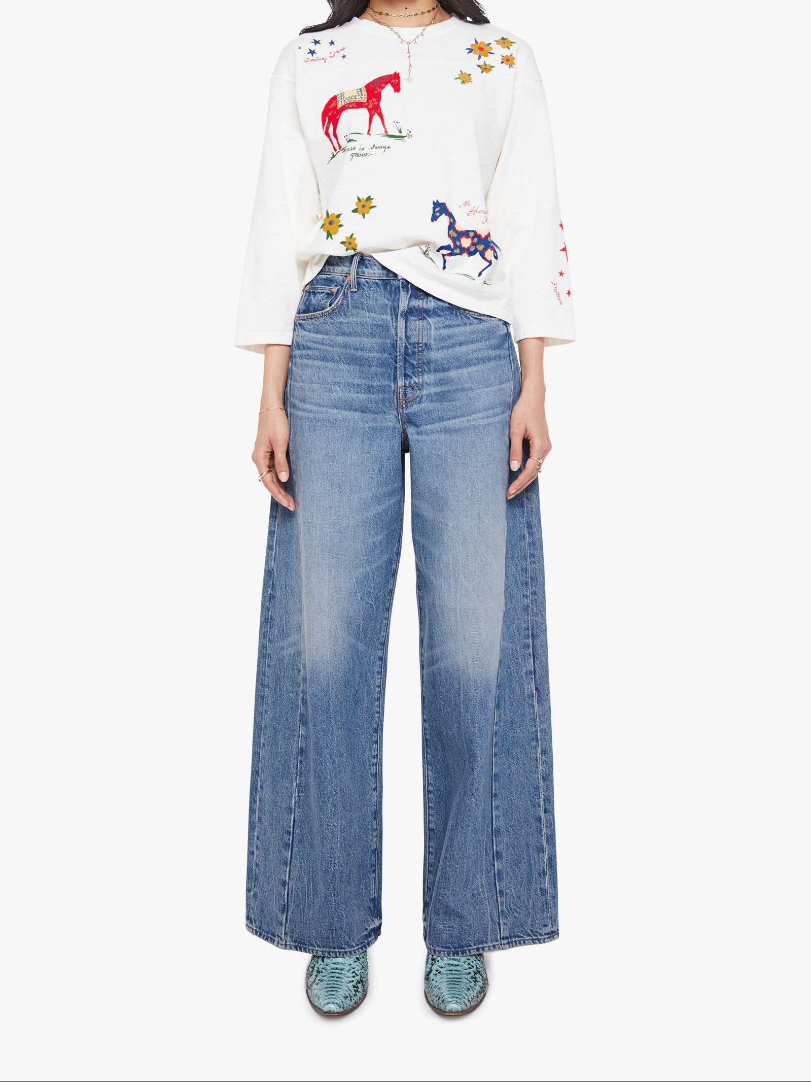 Woman wearing a white shirt with colorful designs and blue jeans on a white background