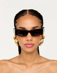 Woman wearing large sunglasses and gold hoop earrings on a plain background