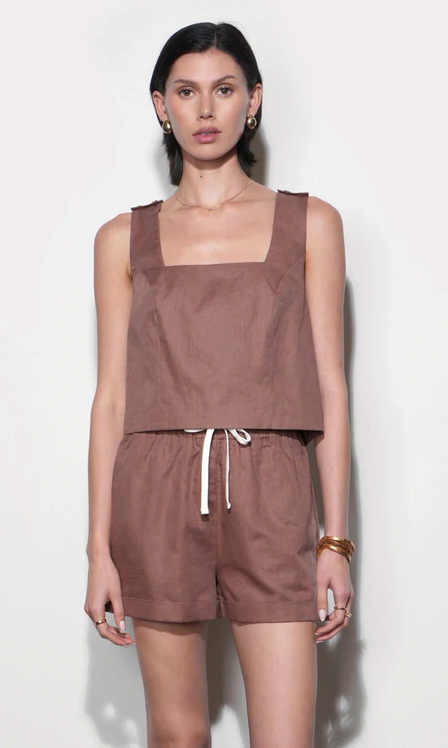 Woman wearing a brown sleeveless top and shorts set against a white background
