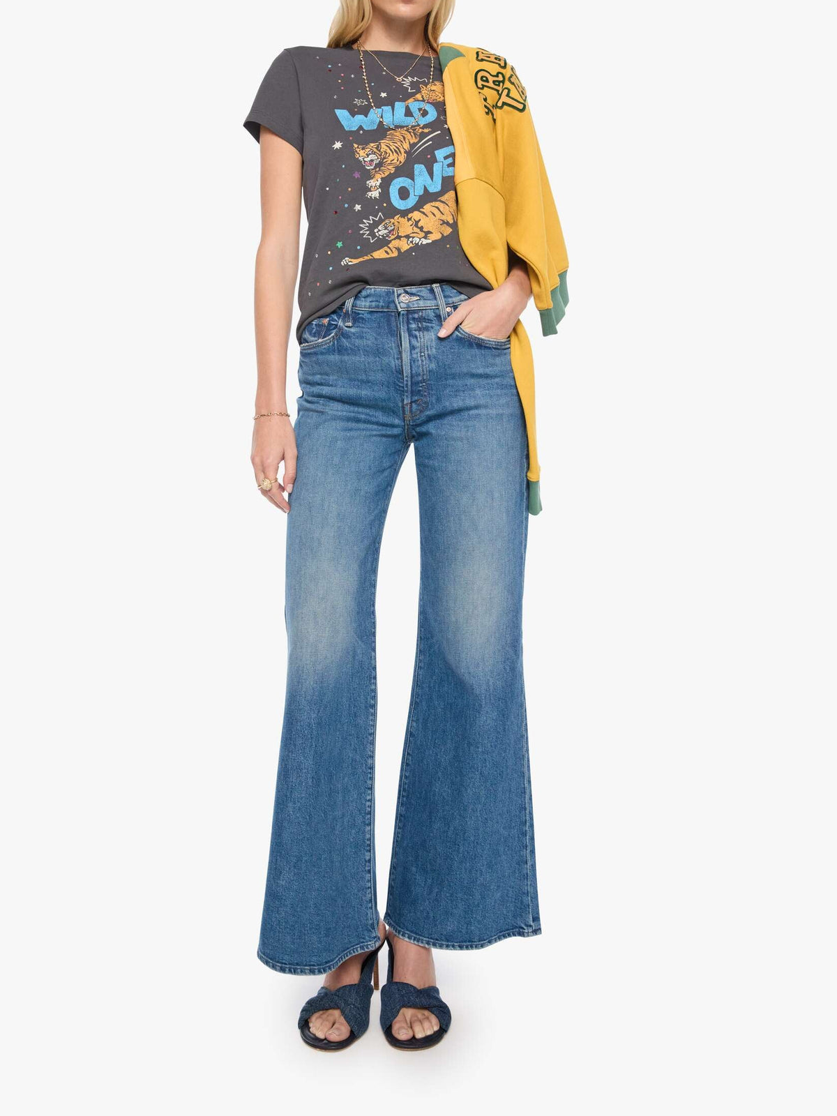 Woman wearing a graphic t-shirt, yellow jacket, and blue jeans on a white background