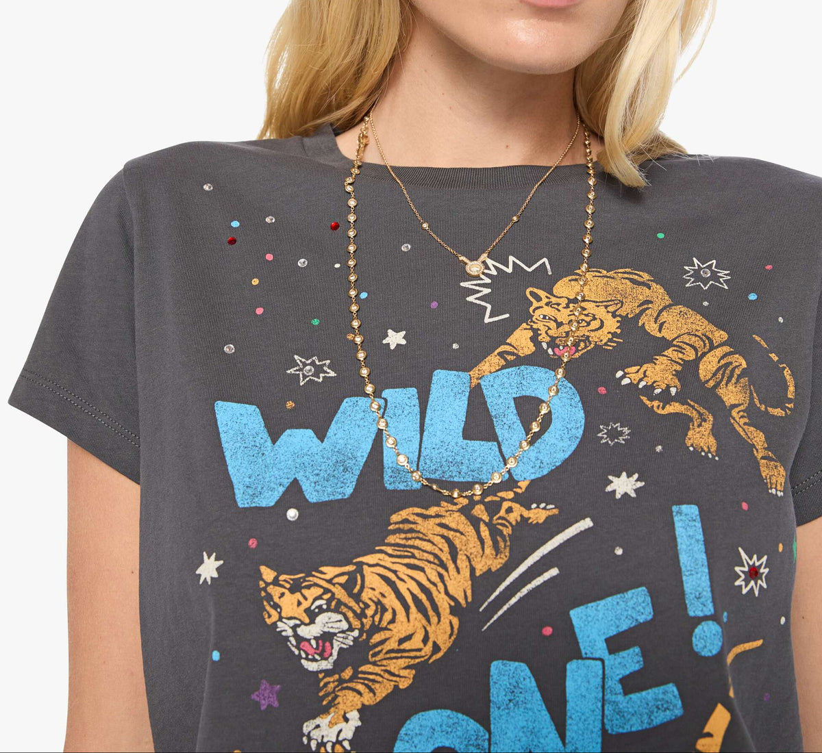 A close-up of a model wearing a dark gray graphic t-shirt with a tiger and the words 'WILD ONE!' in blue and orange, accessorized with layered gold necklaces.