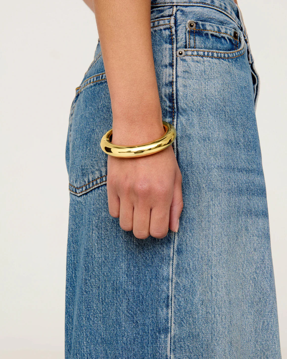 gold bangle bracelet on model wrist with blue jeans on a white background