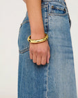 gold bangle bracelet on model wrist with blue jeans on a white background