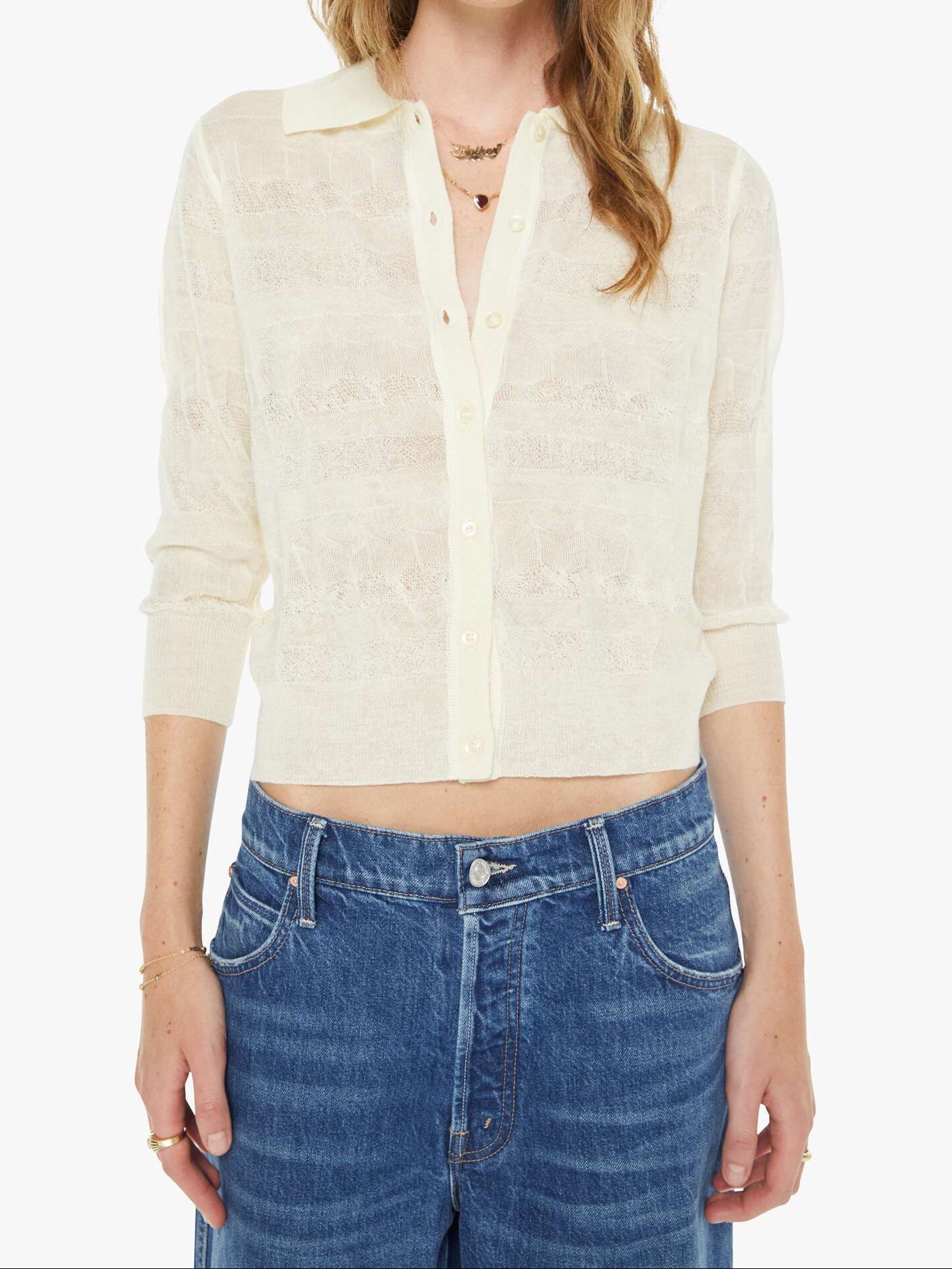 Woman wearing a cream-colored cropped shirt and blue jeans on a white background