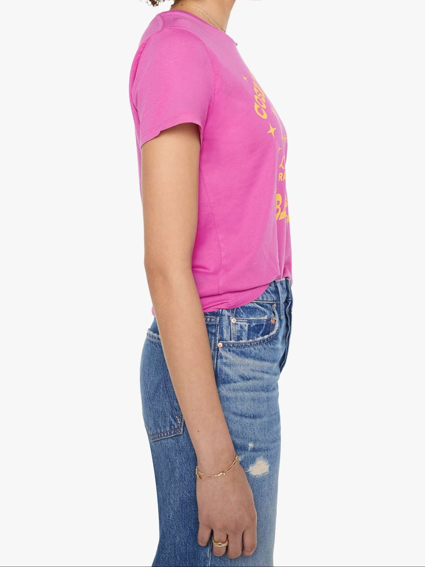 A woman shown in profile wearing a bright pink short-sleeve graphic T-shirt and blue jeans against a plain light gray studio background.