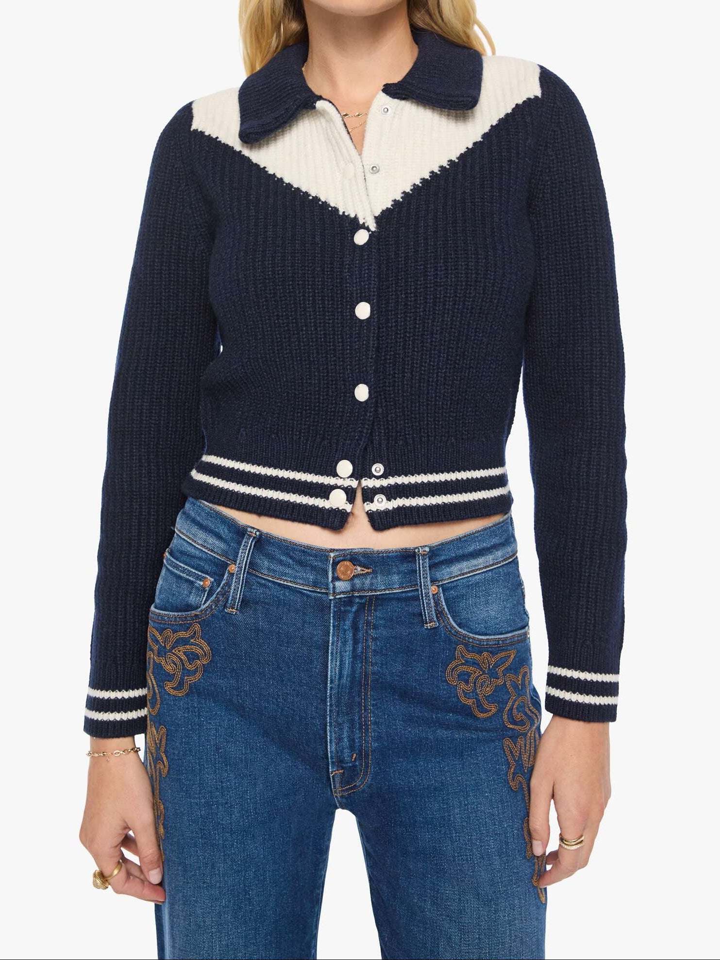 Woman wearing a navy and white cardigan with a white shirt underneath, paired with blue jeans on a white background.