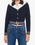 Woman wearing a navy and white cardigan with a white shirt underneath, paired with blue jeans on a white background.