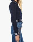 Woman wearing a navy blue sweater with white trim and blue jeans on a white background