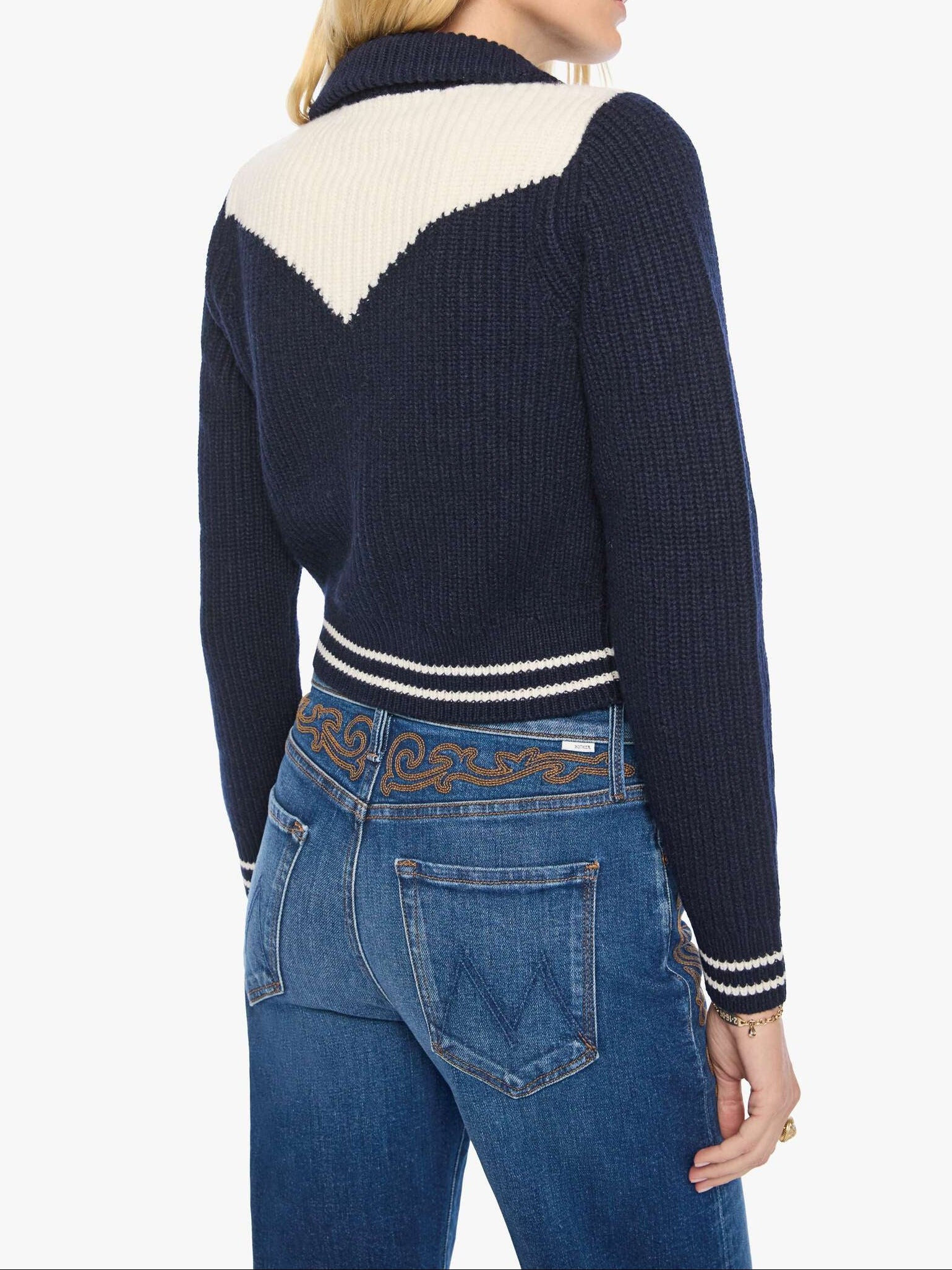 Woman wearing a navy and white sweater with a patterned belt and blue jeans on a white background