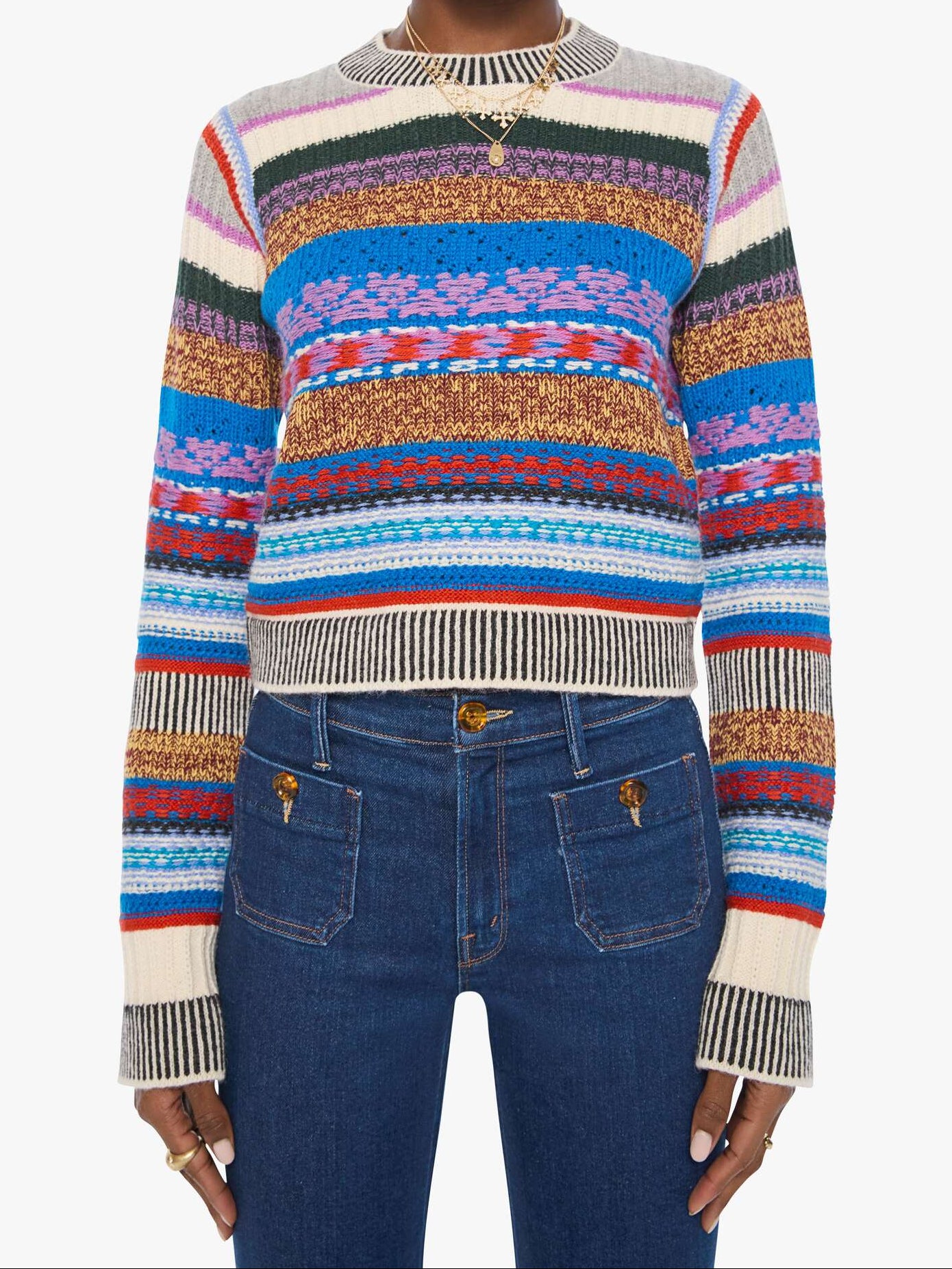 A model wearing a colorful striped knit sweater with horizontal bands of blue, red, orange, yellow, green, and cream, paired with dark blue jeans against a plain white background.