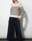 A woman modeling a cream and navy striped knit sweater with wide-leg navy trousers and black ankle boots, standing against a plain light gray wall.