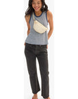 A woman modeling a sleeveless top with thin navy and white horizontal stripes, paired with dark gray jeans, a cream woven crossbody bag, and red flats, set against a plain white studio background.