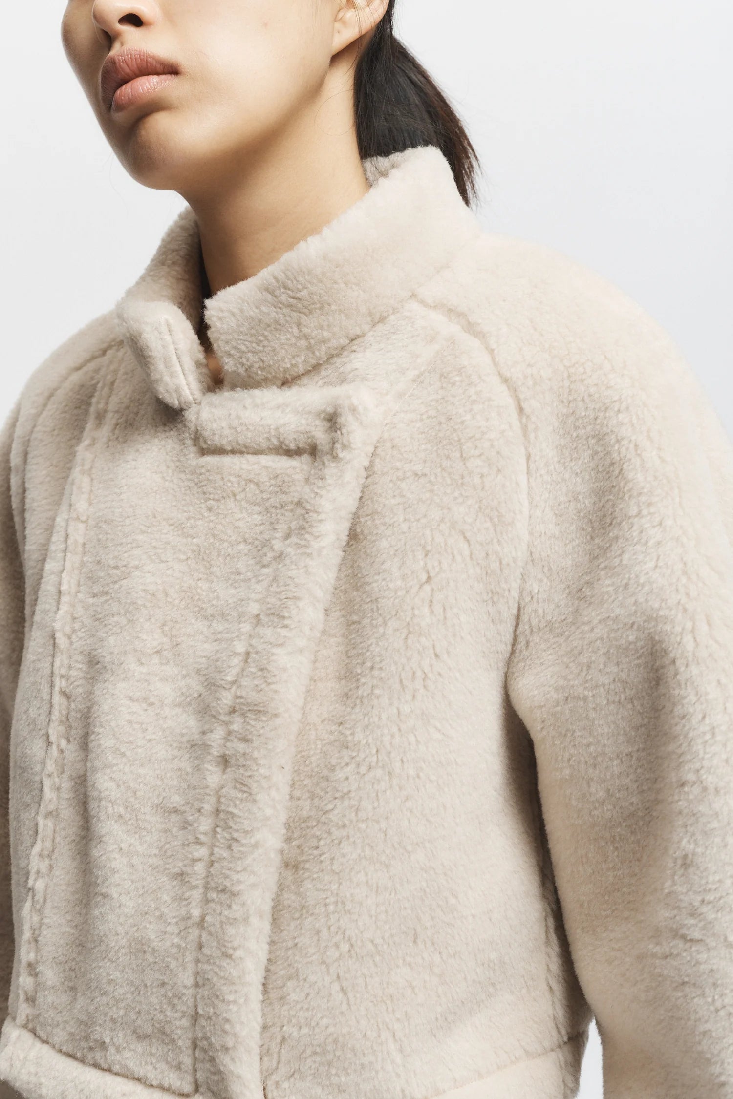 Close-up of a person wearing a beige coat with a neutral background, side view