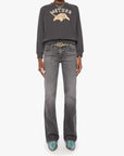 A model stands against a light gray studio background wearing a dark charcoal gray sweatshirt with a gold graphic and the word 'MOTHER' across the chest, paired with faded gray jeans, a decorative belt, and teal shoes.