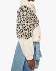 Person wearing a leopard print sweater over a cream turtleneck with a denim jacket on a white background
