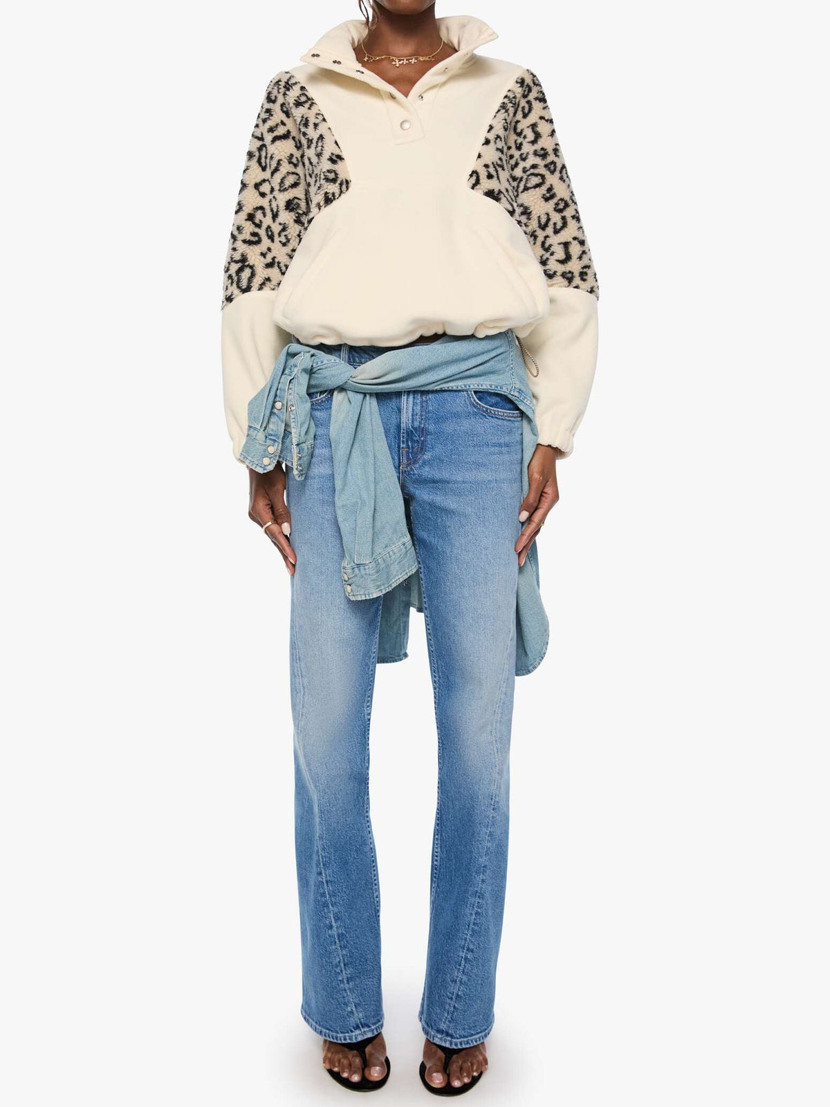 Person wearing a patterned sweater and light blue jeans on a white background