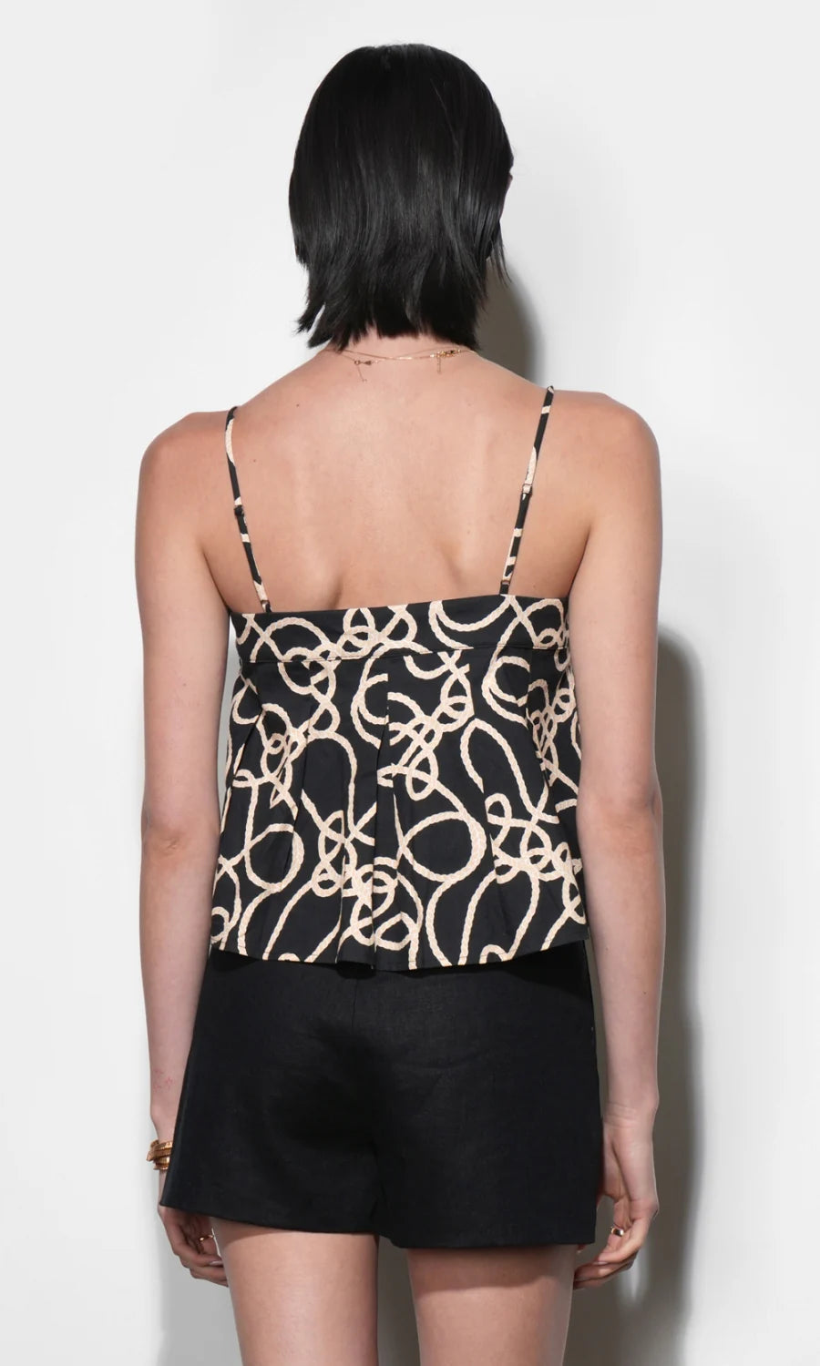 Person wearing a black and beige patterned top with thin straps on a white background