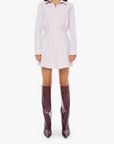 Woman wearing a white shirt dress and brown knee-high boots on a white background