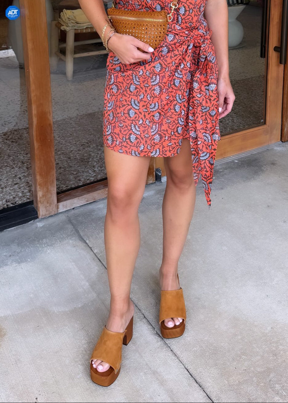 Woman in a red patterned dress standing outside a store with sol sandals
