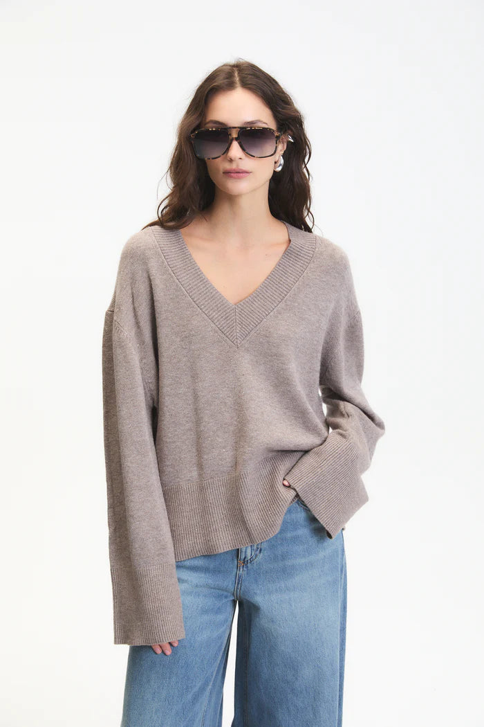 Woman wearing a beige sweater and blue jeans with sunglasses on a white background