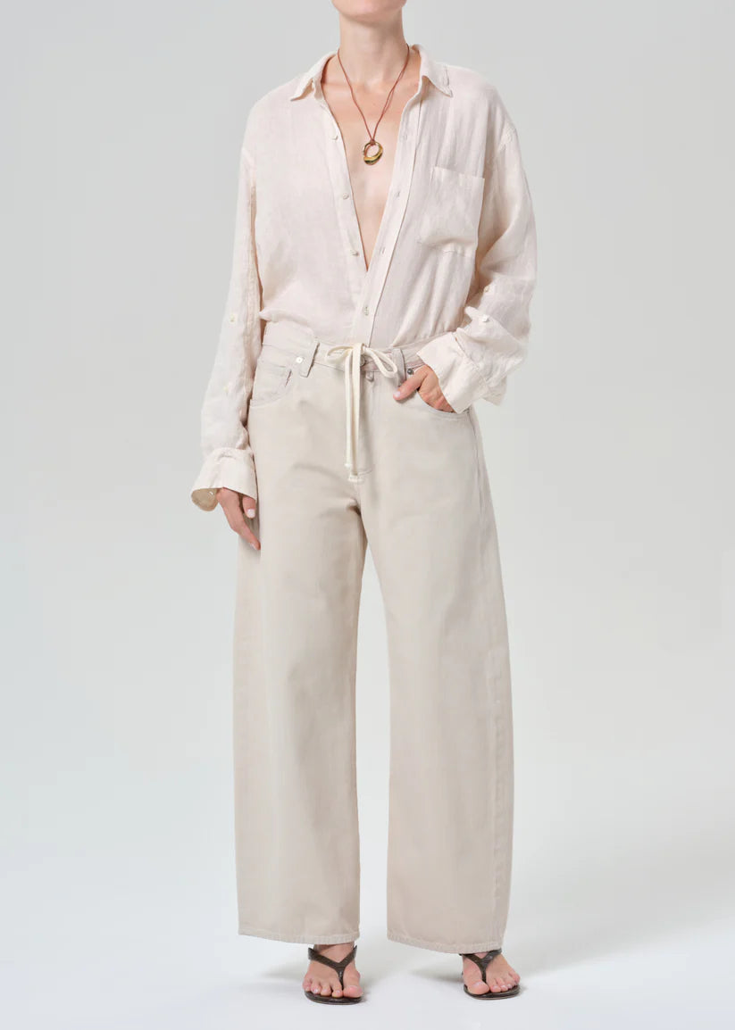 Person wearing a cream button-up shirt and beige pants on a white background